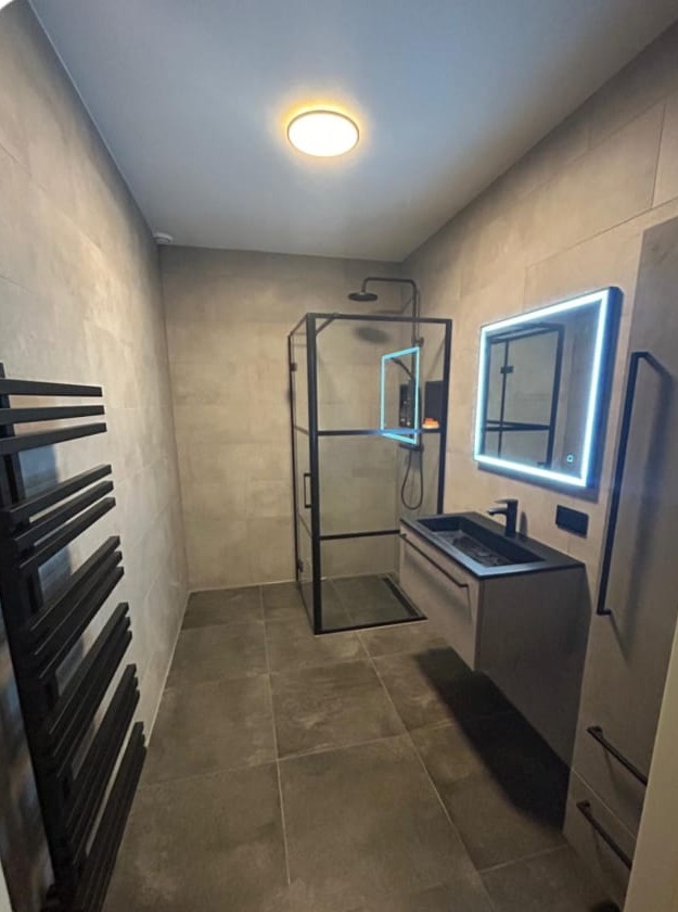 Nieuwe badkamer met inloopdouche met zwart frame, spiegel met verlichting en een zwarte radiator