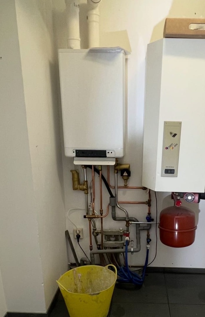 Technische ruimte met een ketel en nieuw leidingwerk aan een witte wand